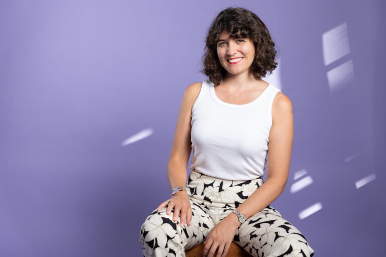 Photo d'Agathe, souriante, assise sur un tabouret.